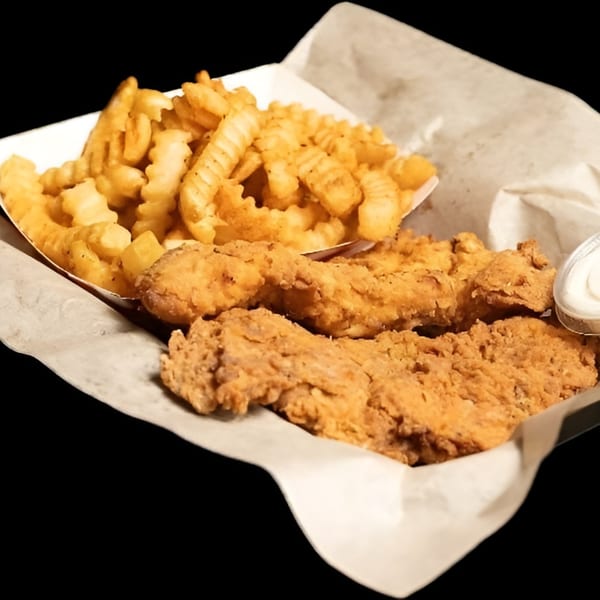 Crispy fried chicken tenders and crinkle-cut fries in a paper-lined basket with a side of dipping sauce.