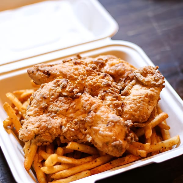 Crispy fried chicken tenders and golden french fries in a white takeout container.