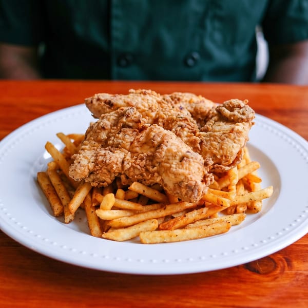 Crispy fried chicken tenders and seasoned french fries on a white plate on a wooden table.