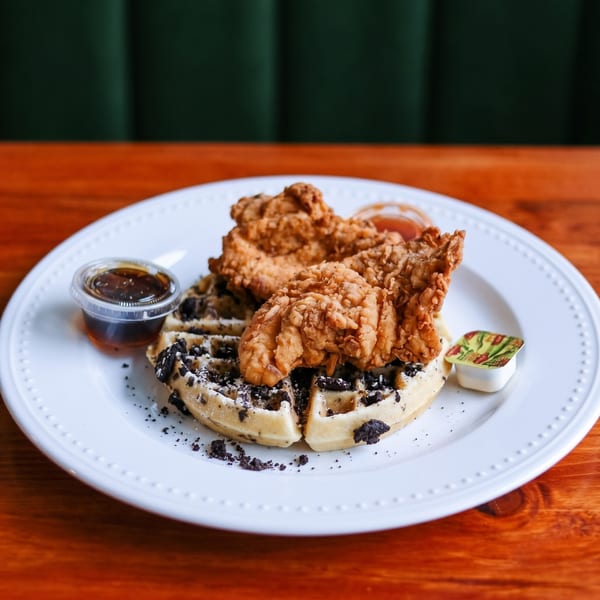 Golden fried chicken tenders on an Oreo waffle with syrup and butter on a white plate.