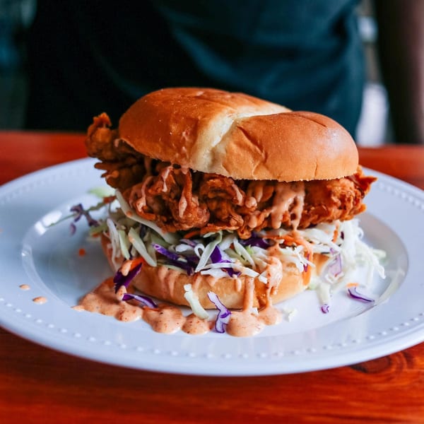 Crispy fried chicken sandwich with coleslaw and sauce on a white plate.