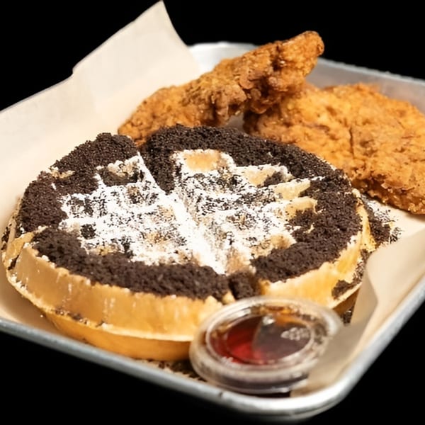 Crispy fried chicken tenders and an Oreo-crusted waffle with powdered sugar and syrup on a tray.